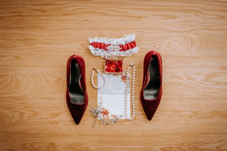 Riga, Latvia - January 20, 2024 - Arrangement of bridal accessories on a wooden floor including red heels, a garter, jewelry, a small floral box, and an ornate hairpiece.