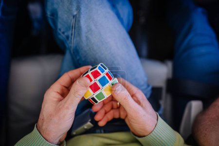 Riga, Letonia - 24 de febrero de 2024 - un individuo sostiene un colorido Cubo de Rubik con un patrón sin resolver. Están sentados, con un traje de mezclilla visible