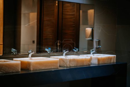 Agadir, Maroc - 25 février 2024 - Éviers en marbre avec robinets en marche, réflexion dans un miroir, éclairage chaleureux et design moderne de salle de bain.
