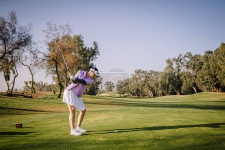 Agadir, Marokko - 25. Februar 2024 - Eine Frau in lila Oberteil und weißem Rock spielt an einem sonnigen Tag Golf