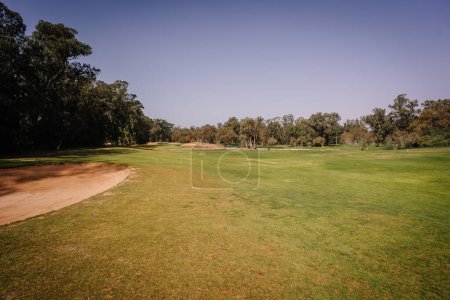 Foto de Agadir, Marruecos - 25 de febrero de 2024 - Vista al campo de golf con un búnker de arena, fairway verde, árboles y cielo azul. - Imagen libre de derechos