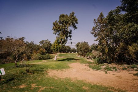 Agadir, Morocco - February 25, 2024 - A scenic view of a golf course with a sandy path, lush trees, and a clear sky.