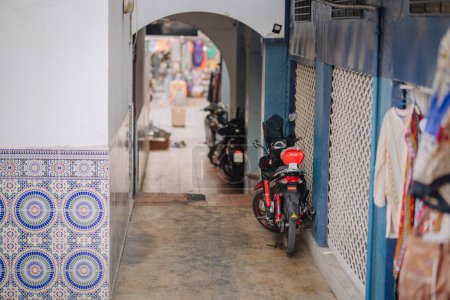 Agadir, Marokko - 25. Februar 2024 - Gasse mit rotem Motorrad, gefliesten Wänden und Kleidung, die auf dem Markt verkauft wird