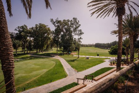 Foto de Agadir, Marruecos - 28 de febrero de 2024 - Vista de un campo de golf con palmeras, hierba verde, cielo despejado y sendero. - Imagen libre de derechos