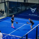 Riga, Latvia - March 3, 2024 - Two male players are focused on the game on an indoor blue padel court with CUPRA branding, as spectators watch from the side