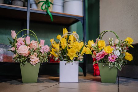 Valmiera, Latvia - March 7, 2024 - three flower arrangements in pastel-colored pots with handles, featuring a mix of yellow daffodils, pink roses, and other florals.