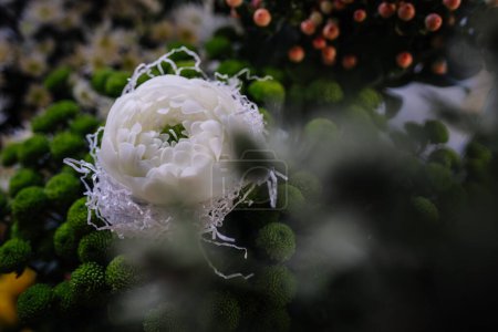 Téléchargez les photos : Valmiera, Lettonie - 7 mars 2024 - Gros plan d'une bougie blanche conçue pour ressembler à une fleur en fleurs, entourée de fleurs sphériques vert foncé et de papier déchiqueté. - en image libre de droit