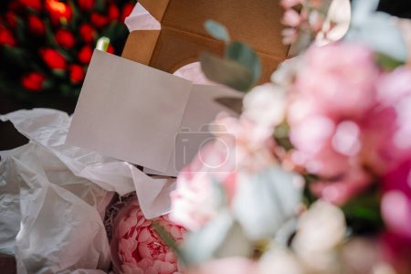 Valmiera, Latvia - March 7, 2024 - A close-up of a floral arrangement with a blank greeting card, surrounded by tissue paper, with colorful flowers blurred in the background.