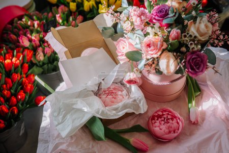 Valmiera, Lettland - 7. März 2024 - Ein lebendiges Blumengesteck in einer rosafarbenen Schachtel mit Tulpen und Rosen, Seidenpapierverpackung und verschiedenen Blumen im Hintergrund in Eimern.
