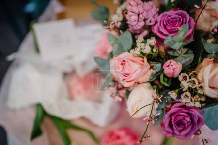 Valmiera, Lettland - 7. März 2024 - Ein lebendiger Strauß aus Rosen und gemischten Blumen, der sich auf eine tiefviolette Rose konzentriert, die von rosa Rosen, Grün und kleinen weißen Blüten umgeben ist, mit einem verschwommenen Hintergrund.