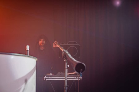 Une cabine DJ avec un équipement de réglage de silhouette à capuchon, un stand de microphone au premier plan, éclairage ambiant, performance, événement, musique, scène.