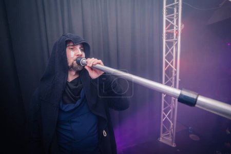 Valmiera, Latvia - March 15, 2024 - A man in a hood plays a tuba-like wind instrument on stage with purple lighting in the background.