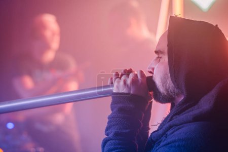 Valmiera, Lettonie - 15 mars 2024 - Un homme de profil joue intensément du didgeridoo, sur fond de scénographie rose floue aux figures floues.