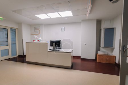 Une réception de l'hôpital avec un bureau, un ordinateur, une armoire et une signalisation sur le mur dans un espace propre et bien éclairé.