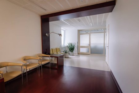 Moderna sala de espera del hospital con sillas, planta, persianas y una lámpara de pie, dando un ambiente limpio y sereno.