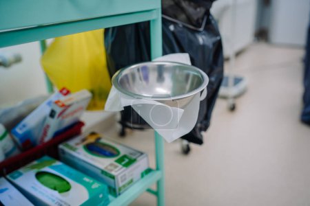 Valmiera, Latvia - March 20, 2024 - A stainless steel kidney dish on a medical trolley, lined with paper towel, likely used for holding sterile instruments or waste materials during medical procedures.