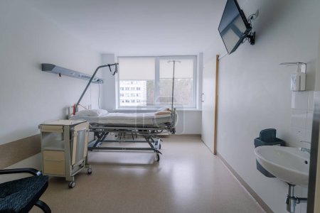 Valmiera, Lettland - 20. März 2024 - Ein Krankenhauszimmer mit einem verstellbaren Bett, einem IV-Stativ, einem Patientenmonitor, einem Händedesinfektionsspender und einem Fenster mit Blick auf ein Gebäude im Freien.