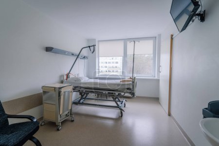 Valmiera, Latvia - March 20, 2024 - A hospital room with an adjustable bed, an IV stand, a patient monitor, a hand sanitizer dispenser, and a window with a view of a building outside.