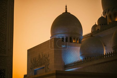 Dubai,  Unite dArab Emirates - October 19, 2019 - Close-up of mosque domes at dusk with lit windows and detailed architecture against a golden sky.