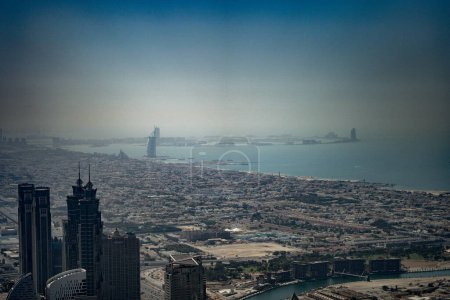 Dubai,  Unite dArab Emirates - October 19, 2019 - A hazy aerial view of a city with skyscrapers and a distinctive sail-shaped building by the coast.