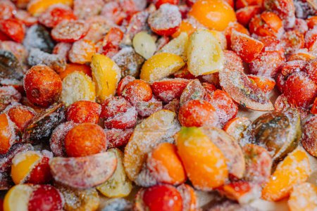 Heap of halved, frosty tomatoes with ice crystals, in a mix of red and yellow colors.