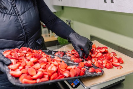 A person is transferring freeze-dried strawberry slices from a baking sheet to a digital scale for weighing.