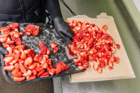 A person is transferring freeze-dried strawberry slices from a baking sheet to a digital scale for weighing.