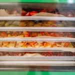 Various fruits and vegetables are spread out on trays inside a freeze dryer.