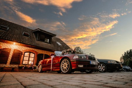 Photo for Valmiera, Latvia - July 8, 2023 - a red wedding car decorated with flowers parked outside a brick building under a sunset sky. - Royalty Free Image