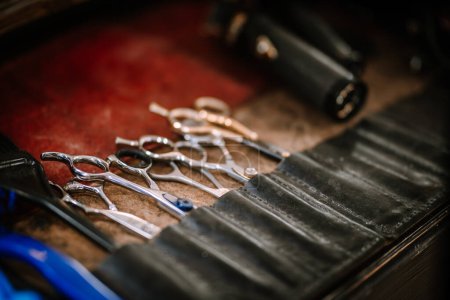 Valmiera, Latvia - Augist 13, 2023 - a close-up of professional hairdressing scissors and clippers neatly arranged in a leather tool roll on a red surface.