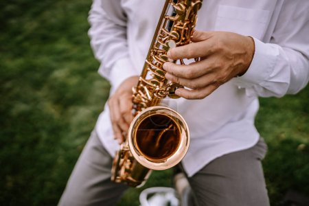 Valmiera, Latvia - Augist 13, 2023 - Close-up of a person playing a golden saxophone, focusing on the hands and instrument against a blurred green background.