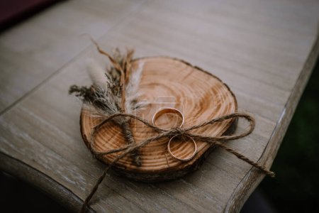 Valmiera, Latvia - Augist 13, 2023 - Two wedding rings rest on a wooden slab, tied together with twine, accompanied by dried flowers, symbolizing unity and natural elegance at a wedding.