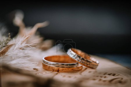 Valmiera, Latvia - Augist 13, 2023 - Close-up of two wedding rings on a textured paper with calligraphy and feather details, emphasizing the intricate designs and the contrast against the wooden surface.