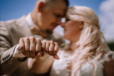 Concentrez-vous sur les mains d'une mariée et d'un marié avec des doigts roses entrelacés, leurs alliances visibles et le doux flou de leurs visages en arrière-plan.