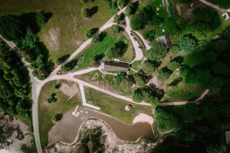 Valmiera, Latvia - Augist 13, 2023 - An overhead shot displays a meandering body of water surrounding a central landmass with pathways and a large structure, amidst verdant terrain.