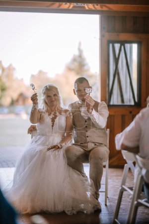Valmiera, Latvia - August 13, 2023 - A bride and groom are sitting together, each holding a whimsical bubble wand, with a soft focus and a warm, backlit interior setting.