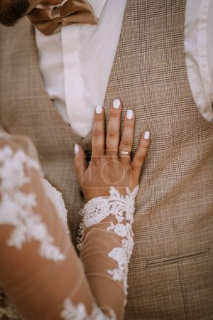 Photo for Valmiera, Latvia - August 13, 2023 - Close-up of a bride's hand with a white lace sleeve and manicured nails resting on a groom's tweed suit, showcasing their wedding rings. - Royalty Free Image