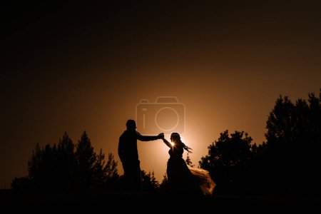 Photo for Valmiera, Latvia - August 13, 2023 -  a bride and groom are silhouetted against a dramatic orange sky at sunset, touching foreheads lovingly with the sun between them. - Royalty Free Image