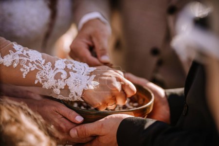 Valmiera, Lettonie - 13 août 2023 - Mains tendues dans un bol, avec une personne portant une manche en dentelle, éventuellement lors d'une cérémonie de mariage.
