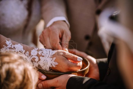 Valmiera, Lettonie - 13 août 2023 - Mains tendues dans un bol, avec une personne portant une manche en dentelle, éventuellement lors d'une cérémonie de mariage.