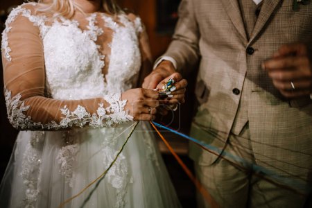 Close-up of a bride and groom's hands as they tie a traditional handfasting cord during their wedding ceremony.
