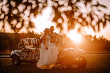 Photo for Valmiera, Latvia - August 13, 2023 - A bride and groom sit on a golf cart with a zebra stripe design at sunset, with trees and a soft glowing sky in the background. - Royalty Free Image