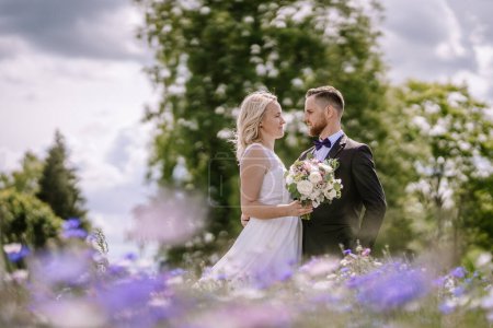Foto de Valmiera, Letonia - 14 de julio de 2023 - Una pareja de novios se encuentran juntos en un campo de flores, mirándose a los ojos bajo un cielo brillante - Imagen libre de derechos