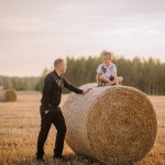 Valmiera, Latvia - August 17, 2024 - A man in business attire smiles at a young boy sitting atop a hay bale in a field at dusk.
