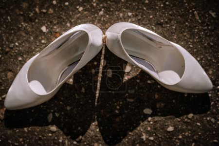 Valmiera, Latvia- July 28, 2024 - A pair of white bridal shoes on a textured surface with a pebble between them.