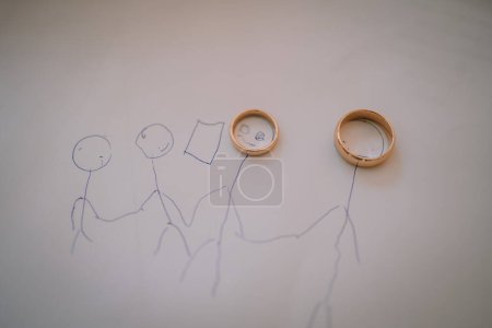 Valmiera, Letonia - 28 de julio de 2024 - Dos anillos de boda colocados en un dibujo de una pareja cogida de la mano.