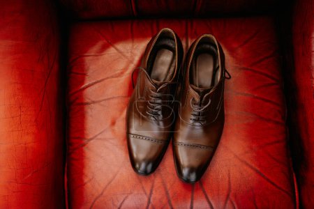 Valmiera, Letonia 28 de julio de 2024 - Los zapatos de vestir de cuero marrón se colocan cuidadosamente sobre un fondo rojo texturizado, probablemente indicativo de un evento formal o un atuendo sofisticado..