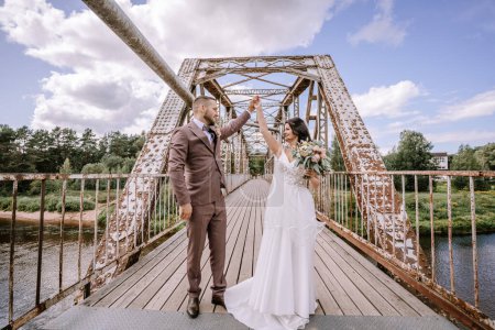 Photo for Valmiera, Latvia- July 28, 2024 -Bride and groom dance on a rustic bridge, the groom holding the bride's hand up in a twirl. - Royalty Free Image