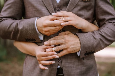 Foto de Valmiera, Letonia - 28 de julio de 2024 - Un primer plano de las manos de una pareja recién casada, mostrando sus anillos de boda, con el novio abrazando a la novia por detrás. - Imagen libre de derechos