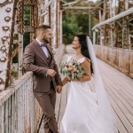 Valmiera, Latvia- July 28, 2024 - A bride and groom smiling at each other on an old bridge, holding hands, with the bride holding a bouquet.